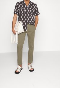 Camicetta nera a maniche corte con motivo bianco; pantaloni verde oliva; sandali bianchi con suola nera; borsa tote beige.