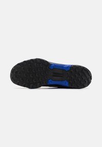 Semelle de chaussure noire et bleue robuste avec un motif de bande de roulement profond, conçue pour offrir de la traction sur différentes surfaces.