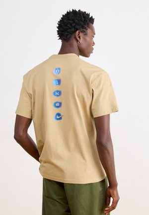 Bakeric t-shirt iz bombaža v bež barvi z okroglim izrezom in kratkimi rokavi. Na hrbtni strani ima grafični napis v modri in beli barvi, ki prikazuje ime blagovne znamke.