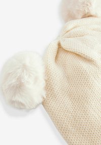 Cappello lavorato a maglia color crema con due morbidi pompon in pelliccia sintetica in cima, che presenta una trama testurizzata e una forma semplice e arrotondata.