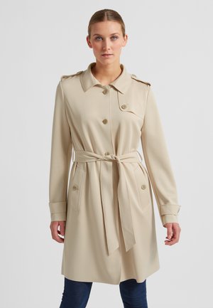 Beige Trenchcoat mit doppelter Knopfblende, großem Kragen und tailliertem Design. Mit Knopfdetails und zwei vorderen Taschen. Glatte Textur.