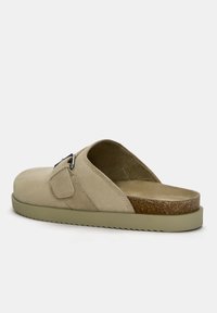 Beige suède instapsandaal met een ronde neus, verstelbare gesp en een gestructureerde kurken voetbed. Heeft een groene rubberen buitenzool.