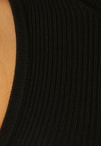 Tessuto a coste nere che mostra la texture con linee orizzontali. Il materiale appare morbido ed elastico. I bordi sono rifiniti in modo ordinato.