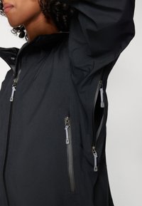 Black waterproof jacket featuring a high collar, multiple zipped pockets, and smooth fabric texture. Zipper pulls in contrasting gray.