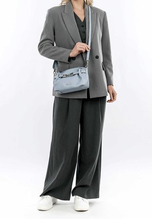 Grijze blazer over een zwarte top, gecombineerd met grijze wijde broek. Houdt een lichtblauwe leren handtas vast met zilveren hardware en schouderband.