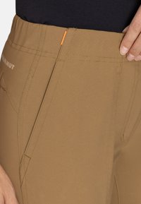 Brązowe spodnie legginsy z dopasowaną talią, skośnymi kieszeniami, pomarańczowym akcentem przy talii i widocznymi detalami szwów.