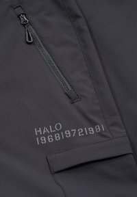 Zwarte stoffen jas met een ritssluiting, een verticale ritstas en een bedrukt logo met cijfers aan de voorkant. Soepele textuur.