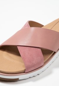 Pink slide sandal featuring cross straps in smooth and suede textures, a cushioned tan footbed, and a white rubber sole.