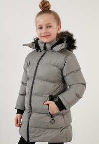 Grå pufferjakke med en blank tekstur, sort kunstpels hætte og lynlåslommer. Har en frontlynlås og ribbede manchetter for varme.