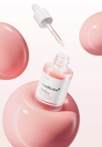 Bottiglia di siero rosa con contagocce bianco, etichetta con testo chiaro, circondata da forme rosa lucide su uno sfondo sfumato.