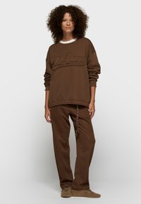 Sweat-shirt marron surdimensionné avec logo texturé, accompagné d'un pantalon assorti à coupe décontractée avec cordon de serrage. Tissu doux et confortable.