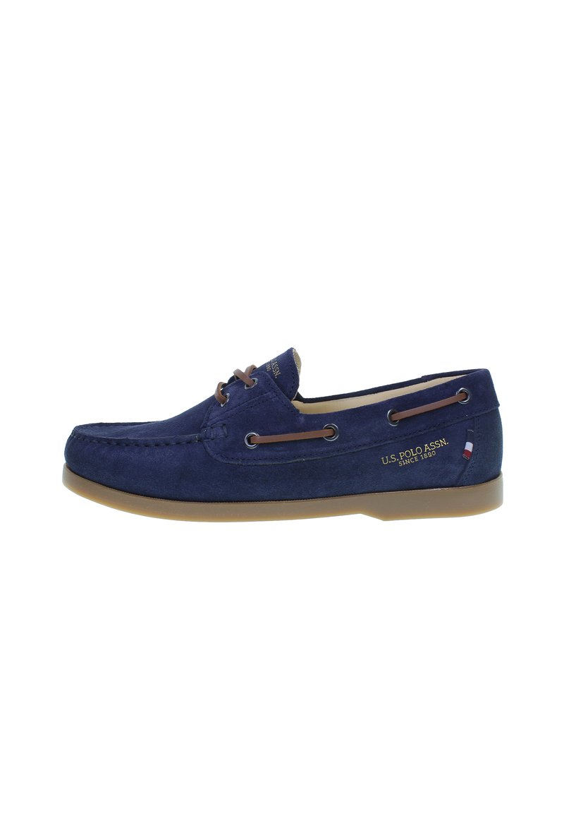 Zapato de barco de ante azul marino con cordones de cuero, suela de goma y detalles del logotipo en dorado. Los acentos laterales incluyen un pequeño emblema de bandera.