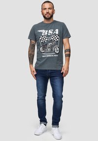 Grå T-shirt med BSA-grafik, rund hals og korte ærmer. Parret med mørkeblå jeans og hvide sneakers. Casual fit og bomuldsstof.