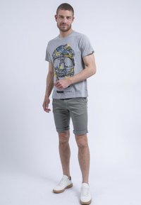T-shirt graphique gris avec texte et motif colorés, associé à un short gris retroussé et des baskets blanches avec une semelle beige.
