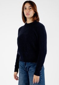 Maglione in maglia tessuta blu navy, con scollo rotondo e maniche lunghe, abbinato a jeans azzurri. Design semplice e vestibilità casual.