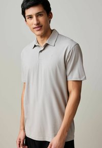 Polo shirt grigio chiaro realizzato in tessuto morbido, con colletto classico, due bottoni e un piccolo logo sul petto. Maniche corte.