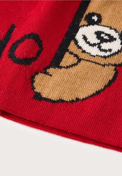 Tissu tricoté rouge avec un visage d'ours brun souriant et une partie de lettres noires sur le côté gauche.
