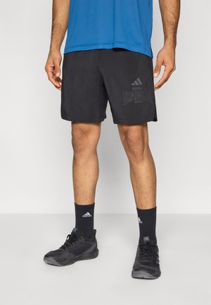 Mustat urheilushortsit teksturoidulla pinnalla, joissa on "Adidas Training Club" -logo, yhdistettynä mustiin sukkiin ja treenikenkiin.