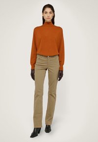 Suéter de cuello alto en color óxido, pantalones rectos beige, guantes marrones y botines negros de tacón. Diseño sencillo, textura suave y tonos neutros.