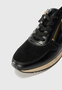 Basket noire avec un mélange de cuir et de textures en suède, lacets noirs plats et détail de fermeture éclair dorée, présentant une semelle légère.