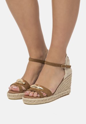 Sandalias cuña de ante marrón con tacón de yute tejido, diseño de punta abierta, detalle dorado en las correas y hebilla ajustable en el tobillo.