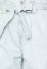 Jasnoniebieskie dżinsy z przewiązanym paskiem w talii, kilkoma przeszyciami oraz pojedynczym guzikiem z przodu.