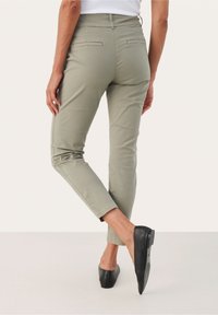 Un pantalon slim-fit vert clair avec taille haute, poches arrière et ourlets retournés, associé à des chaussures noires à enfiler. Texture de tissu lisse.