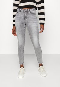Jeans ajustados grises con un lavado desgastado, cinco bolsillos y trabillas para cinturón, combinados con zapatillas blancas y un suéter a rayas negro y crema.
