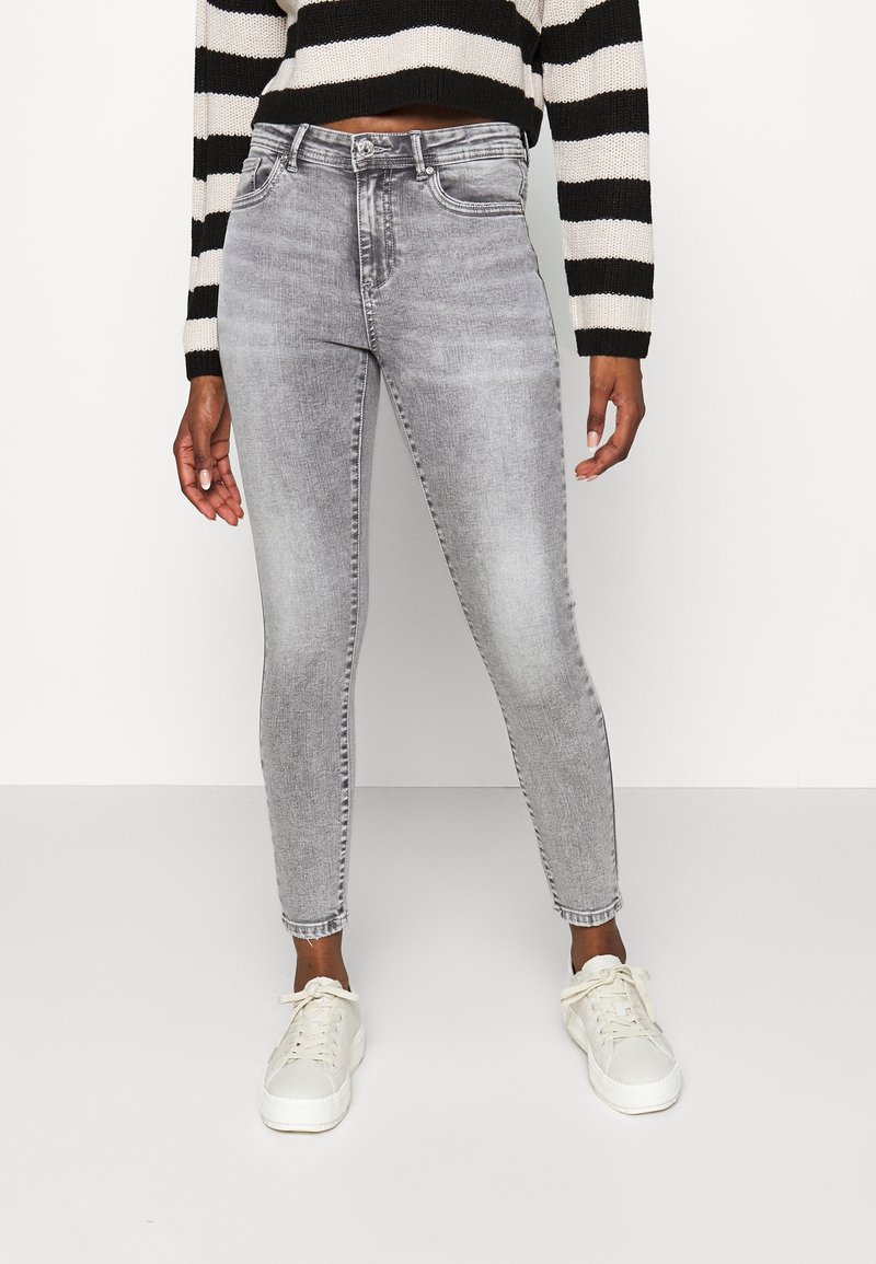Jeans ajustados grises con un lavado desgastado, cinco bolsillos y trabillas para cinturón, combinados con zapatillas blancas y un suéter a rayas negro y crema.