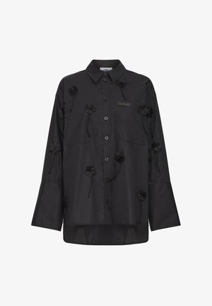 Čierna košeľa s dlhými rukávmi na gombíky, s ostrým golierom, zdobená malými čiernymi kvetinovými aplikáciami rozptýlenými po prednej strane a rukávoch.