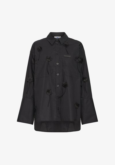 Sort langærmet skjorte med knapper og spidst krave, dekoreret med små sorte blomsterapplikationer spredt på fronten og ærmerne.