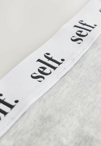Sivi materijal s teksturalnom završnom obradom, s bijelim strukom označenim s "self." u crnom tekstu koji se ponavlja. Prikaz iz blizine naglašava materijale i dizajn.