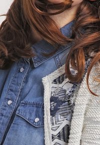 Chemise en denim avec un design à boutons, dotée d'un col intérieur à motifs. Superposée avec un cardigan gris texturé, mettant en valeur un motif tissé.