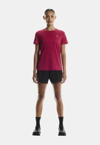 Rdeča kratka športna majica s kratkimi rokavi in krožnim ovratnikom, v kombinaciji z črnimi kratkimi hlačami in črnimi nogavicami. Ima logotip na prsih.