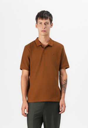 Polo à manches courtes en marron avec un tissu texturé, présentant un col et un patte de boutonnage à deux boutons, associé à un pantalon vert foncé.