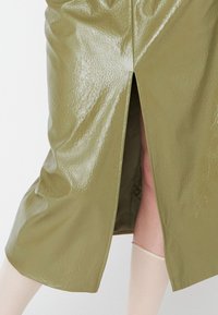Jupe en crayon verte brillante avec une fente sur le côté, forme ajustée, matériau texturé et finition lisse. Le détail de couture exposé ajoute de la dimension.