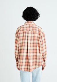Ternet flannel-skjorte i orange, creme og grønne farver. Har lange ærmer, knapmanchetter og en rygsøm for ekstra design.