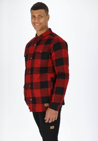 Röd och svart rutigt flanellskjorta med knapprad fram, två bröstfickor och sidfickor, tillsammans med svarta byxor som har diskret varumärke.