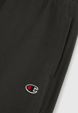 Pantalones jogger de algodón negros con textura acanalada, que presentan un pequeño logotipo bordado en rojo y blanco en el lado izquierdo.