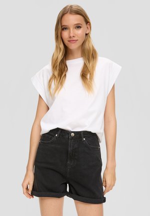 T-shirt blanc oversize avec des manches roulées, associé à un short en denim noir taille haute avec une fermeture à bouton et des ourlets retournés.