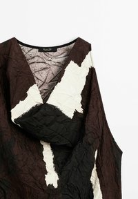 Robe en tissu froissé avec un motif abstrait marron, noir et blanc, col en V et manches longues, étalée à plat sur un fond blanc.