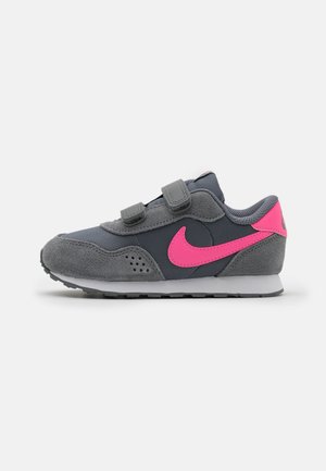 Zapatilla deportiva gris con acentos rosas, que combina materiales de ante y sintéticos, con dos tiras de Velcro y una suela texturizada.
