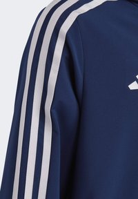 Marineblaue Sportjacke mit drei weißen Streifen auf der Schulter, aus einem glatten Stoff gefertigt, mit taillierter Passform und dezenten Nähten.