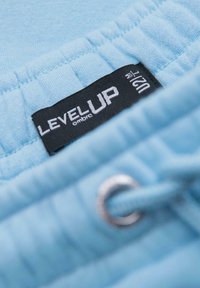 Světle modrá sportovní tkanina s černým štítkem a bílým nápisem "LEVEL UP" a "ombre", připevněná kroužkem z mosazi a šňůrkou.