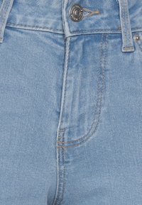 Jeans de denim azul claro com uma cintura alta, apresentando um fecho de correr, fecho de botão e costura reforçada ao longo dos bolsos.
