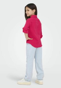 Camisa de manga larga fucsia con mangas enrolladas, combinada con unos vaqueros anchos desgastados de color azul claro y zapatillas blancas.