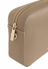 Beżowa torba z teksturowanej skóry z złotym zamkiem, prostokątnym kształtem i małą metalową zawieszką przypiętą do suwaka.