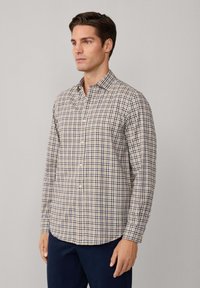 Camisa de cuadros en beige, azul marino y crema; cuenta con un cuello, mangas largas y un dobladillo curvado, hecha de tela ligera.