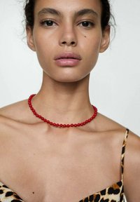 Colier din mărgele roșii pe pielea goală, purtat cu un top cu imprimeu de leopard. Textură netedă, formă circulară și dimensiune uniformă a mărgelei. Design simplu.