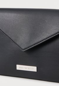 Černá kožená obálková kabelka s diagonálním klopou, stříbrnou logovou destičkou, hladkou texturou a čistými liniemi. Obsahuje minimální hardwarové prvky a akcenty.